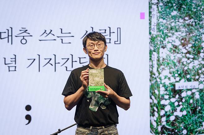 밴드 ‘브로콜리너마저’ 보컬인 윤덕원이 첫 산문집 출간 기자 간담회에서 책을 들고 포즈를 취하고 있다. <민음사>