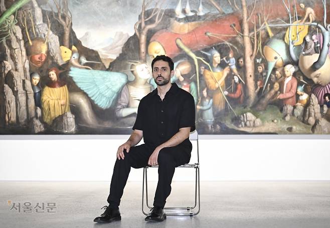 이탈리아 현대미술 작가 알레산드로 시치올드르가 1일 자신의 첫 한국 개인전 ‘고요한 빛, 황홀의 틈’이 열리는 경기 과천 호반아트리움을 찾아 2020년부터 4년에 걸쳐 그린 ‘바보들의 노래’ 앞에 앉아 카메라를 응시하고 있다. 고전 회화의 형식을 빌려 몽환적이고 신비로운 장면을 구현해 내는 작가는 “예술가는 무의식과 현실을 잇는 매개적 존재”라고 말했다. 이지훈 기자