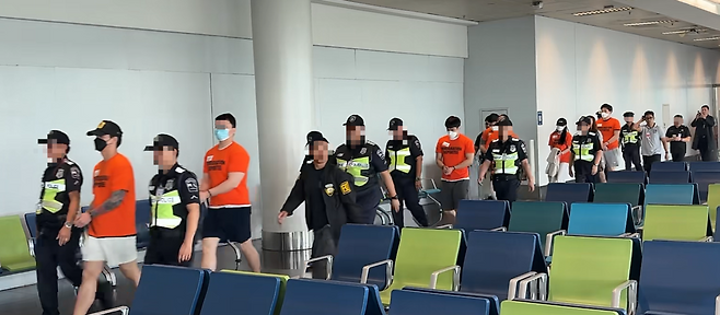 필리핀으로 도망쳤다가 붙잡힌 47명의 범죄 피의자들이 3일 오전 필리핀 마닐라 니노이아키노 국제공항에서 한국으로 강제송환되는 전세기에 탑승하기 위해 현지 경찰에 호송되고 있다. 주화액 반팔티를 입은 이들이 강제 송환되는 피의자들이다. 경찰청 제공