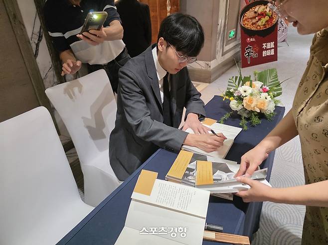 신진서 9단이 지난 2일 중국 칭다오 쉐라톤 칭다오 자오저우 호텔에서 열린 제27회 농심신라면배 세계바둑최강전 사전 기자회견이 끝난 뒤 팬들이 가져온 자서전에 사인을 하고 있다.      칭다오 | 윤은용 기자