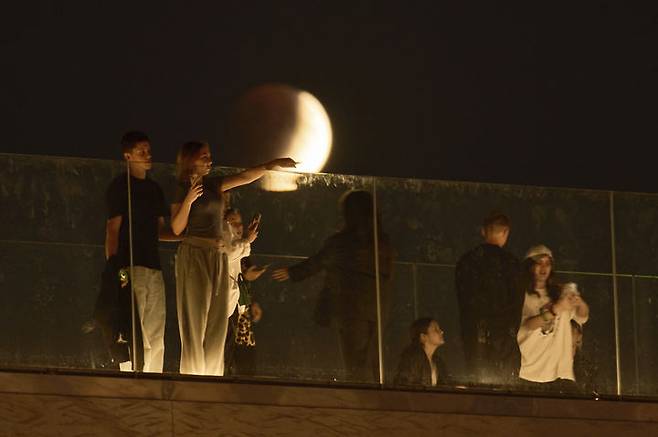 [모스크바=AP/뉴시스] 7일(현지 시간) 러시아 모스크바 자랴디예 공원에서 시민들이 산책을 즐기는 동안 개기월식이 진행되고 있다. '개기월식'은 달이 지구 그림자에 완전히 가려지는 천문 현상이다. 2025.09.08.