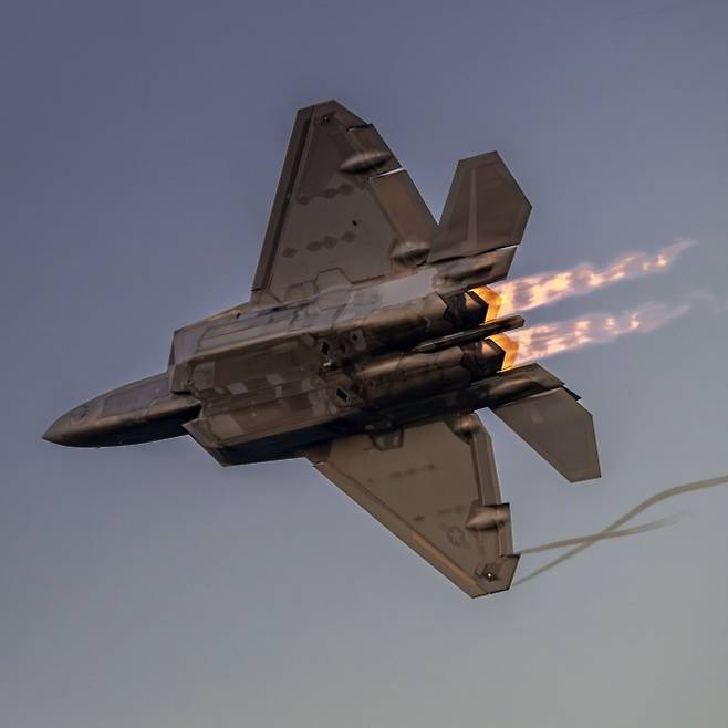 노을빛 하늘을 가르며 애프터버너 화염을 분출하는 F-22 랩터. 미 국방부 제공