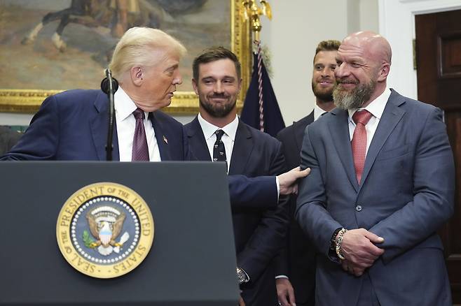 도널드 트럼프 미 대통령이 지난달 31일(현지시간) 백악관에서 진행한 ‘스포츠·건강·영양에 관한 대통령 자문위원회’를 재설립하는 내용의 행정명령 서명식에서 트리플H(56·본명 폴 마이클 레브스크)를 소개하며 그의 팔을 잠시 만지고 있다. [AP]