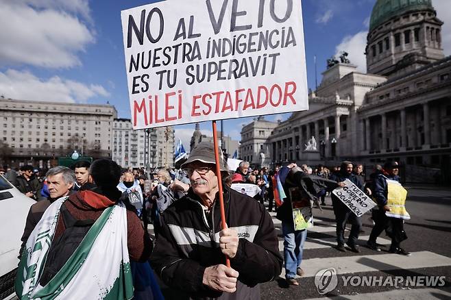 아르헨티나 국회 앞에서 시위하는 은퇴자 [부에노스아이레스=EPA 연합뉴스 자료사진 재판매 및 DB금지] 8월 13일(현지시간) 아르헨티나 부에노스아이레스 국회 앞에서 시위하는 은퇴자가 '(대통령) 거부권에 반대. 우리의 가난은 당신의 재정 흑자. 밀레이 사기꾼'이라는 문구가 적힌 푯말을 들고 있다. 아르헨티나 하비에르 밀레이 대통령이 연금 인상 법안에 거부권을 행사한 후, 아르헨티나 은퇴연금 수령자들은 이에 반대하는 시위를 꾸준히 이어왔다.