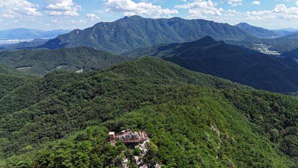 경북 김천시 아포읍 제석봉 정상에서 드론을 날려 담은 풍경이다. 정상에는 돌탑과 산불초소가 있고 그 주위에 나무 덱을 설치한 덕에 이곳에 서면 동서남북으로 조망이 활짝 열린다. 사진 가운데 누워 있는 부처님 얼굴 형상을 한, 구미의 진산인 금오산이 우뚝하다. 오른쪽으로 영암산이 보인다.