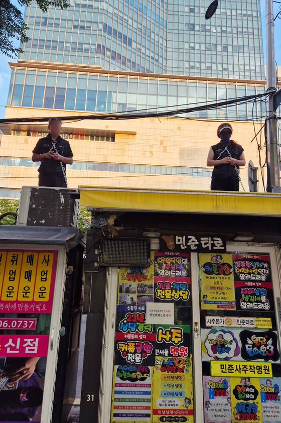 지난 10일 건대입구역 2번출구 앞 노점 박스 위에서 노점상 조합원들이 몸에 쇠사슬을 두르고 광진구청의 노점 철거에 대한 항의를 이어가고 있다. 페이스북 캡처