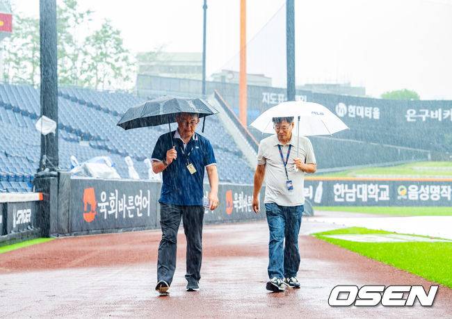 [OSEN=대전, 민경훈 기자] 28일 오후 대전 한화생명볼파크에서 2025 신한 SOL Bank KBO리그 한화 이글스와 LG 트윈스의 경기가 열릴 예정이지만 그라운드에 비가 내리고 있다.이날 새벽부터 대전 지역에 내린 비가 오전에도 멈추지 않고 있다. 오전 11시 기준으로 시간당 6.8mm 적잖은 강수량을 보이고 있다. 내야에 대형 방수포를 깔았지만 외야와 나머지 그라운드는 빗물로 젖었다.박종훈 감독관(왼쪽)이 그라운드 상태를 보고 있다. 2025.09.28 /rumi@osen.co.kr