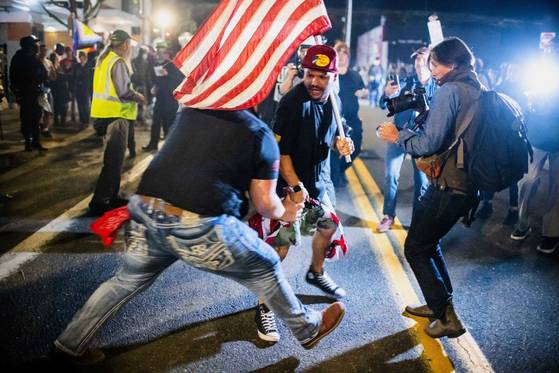 트럼프 지지자(가운데)가 지난 6일(현지시간) 미국 오리건주 포틀랜드의 미국 이민세관단속국 시설 밖에서 시위 도중 불타는 성조기를 놓고 한 시위대와 몸싸움을 벌이고 있다. AP=연합뉴스