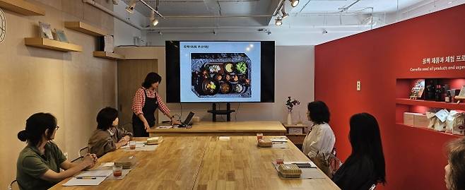 서귀포시 남원읍 신흥2리 동백마을 주민들이 동백언우재에서 2박 3일 은퇴자마을 체험 프로그램 참가자를 대상으로 동백기름으로 만든 요리들을 소개하고 동백 오일이 들어간 차롱에 담긴 샌드위치를 시식하려고 하고 있다. 제주 강동삼 기자