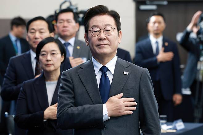 President Lee Jae Myung (center) looks on to the national flag during the opening ceremony of the biennial Seoul ADEX 2025 in Goyang, Gyeonggi Province, Monday. (Pool photo via Yonhap)