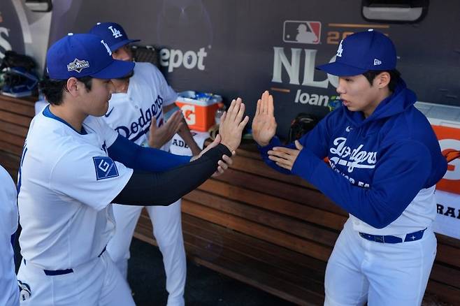 로스앤젤레스(LA) 다저스의 오타니 쇼헤이(왼쪽)가 15일(현지 시간) 미 캘리포니아주 로스앤젤레스의 다저 스타디움에서 열리는 2025 메이저리그 내셔널리그 챔피언십 시리즈(NLCS·7전4선승제) 3차전 밀워키 브루어스와 경기를 준비하면서 더그아웃에서 김혜성과 하이 파이브를 하고 있다. 김혜성은 NLCS 엔트리에 포함됐지만 경기에는 나서지 못하고 있다. 뉴시스