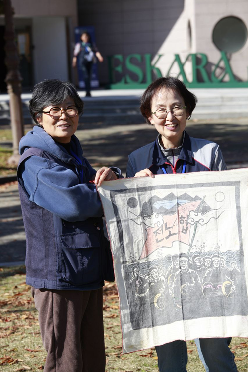 1990년 1월22일, 수원 성균관대학교에서 열린 전국노동조합협의회(전노협) 창립대회 당시 제작했던 천 포스터를 들고 창립식 현장에 있었던 이선희(왼쪽) 민주노총 경기도본부 총무국장과 조귀제 민주노총 경기도본부 부본부장이 행사가 열렸던 건물 앞에서 기념 촬영을 하고 있다. /민주노총 경기도본부 제공