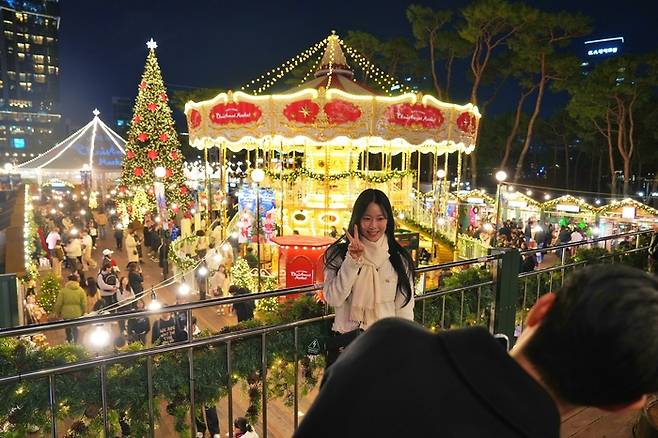 롯데타운 잠실 ‘크리스마스 마켓’에서 ‘2층 회전목마’와 ‘초대형 크리스마스 트리’ 를 배경으로 사진을 찍는 모델. [롯데백화점]
