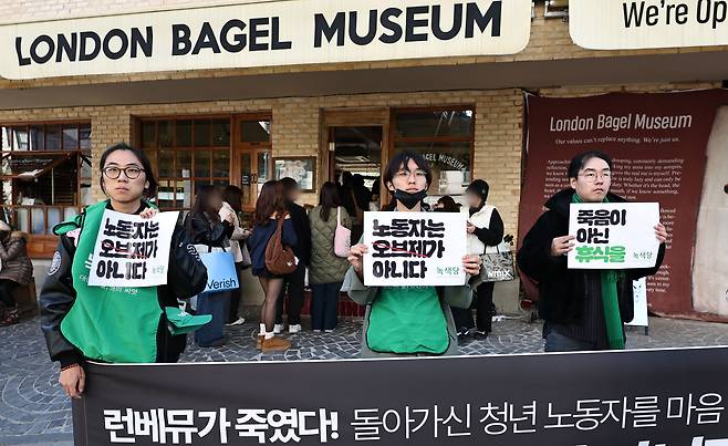 Members of the Green Party hold placards during a party address on the death of a London Bagel Museum worker outside the chain’s Anguk branch in Jongno District, central Seoul, on Nov. 3. [YONHAP]