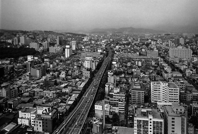 쁘렝땅 백화점(현 장교빌딩) 옥상에서 바라본 저녁 청계천 전경. 가운데 청계천을 따라 세워진 삼일고가를 중심으로 왼쪽으로 종로와 오른쪽으로 을지로가 나란하다. 중간에 좌에서 우로 가로지른 세운상가와 멀리 용마산과 아차산이 보인다. 청계2가, 1989.
