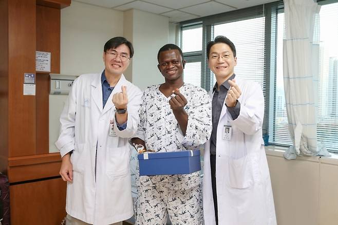 서울아산병원에서 대퇴골 재건 및 피부 이식 수술을 받은 존 콘테 씨(가운데)가 13일 의료진과 기념사진을 찍고 있다. 왼쪽이 서울아산병원 정형외과 김지완 교수, 오른쪽이 성형외과 권진근 교수. [사진=서울아산병원]