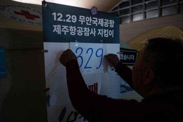 박인욱(70)씨가 22일 새벽 전남 무안국제공항 유가족 쉘터 가장자리에 하늘색 숫자 329가 쓰인 종이를 봍이고 있다. 박씨는 지난 참사로 아내와 딸, 사위 그리고 두 손주를 잃었다. 무안=하상윤 기자