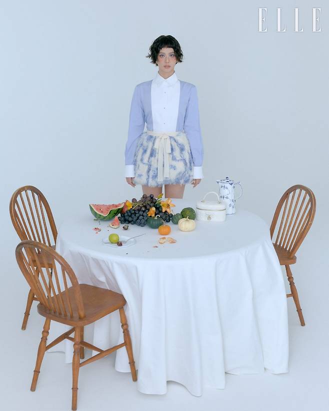 지수가 입은 코튼 포플린 셔츠와 플로럴 모티프의 실크 니트 버블 스커트, 라떼 컬리 램스킨 레더 미니 베니티 케이스는 Dior.