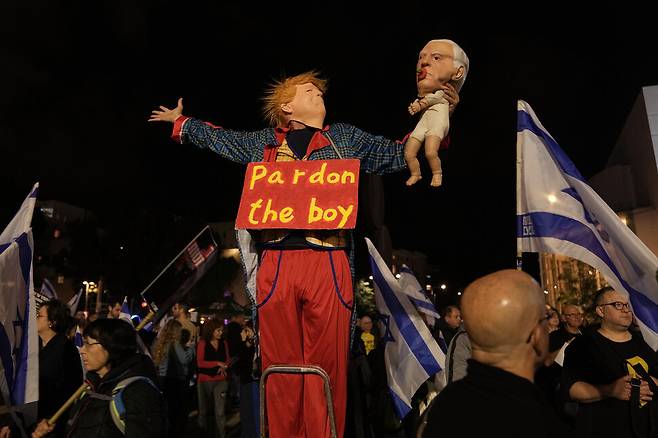 15일(현지시각) 이스라엘 텔아비브 하비마 광장에서 네타냐후 정부를 비판하는 시위대가 2023년 10월 하마스 침입에 대한 네타냐후 총리의 책임을 밝힐 국가조사위원회 구성을 요구하며 시위를 벌이고 있다. 트럼프 대통령으로 가장한 한 시위자가 네타냐후 총리의 가면을 씌운 아기 인형을 들고, 트럼프 대통령이 네타냐후 총리의 사면을 요청한 것을 조롱하고 있다. AP 연합뉴스