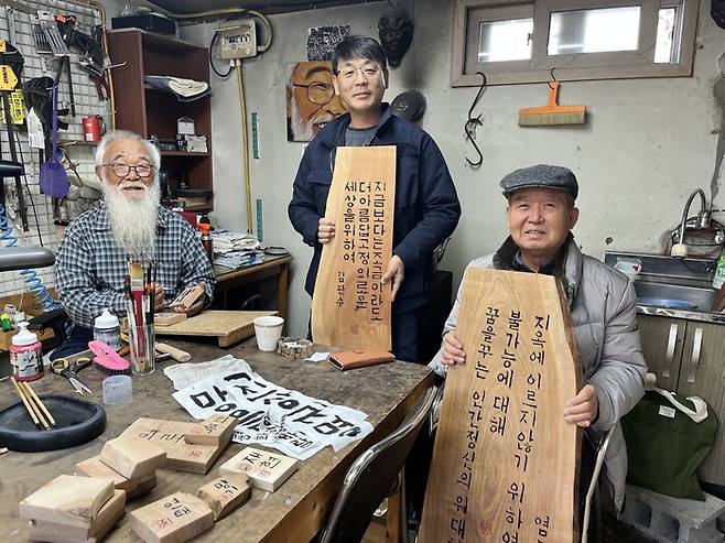 송경동(가운데) 상임이사가 문정현(왼쪽) 신부가 새겨 재단에 기증한 서각을 들고 있는 모습. 오른쪽은 강형철 한국작가회의 이사장.                                                                  송경동 상임이사 제공