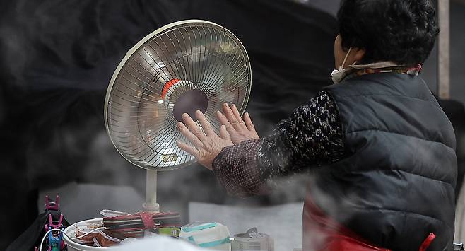A market stall owner warms her hands in front of a heater at a traditional market in Daegu on Dec. 3. [YONHAP]