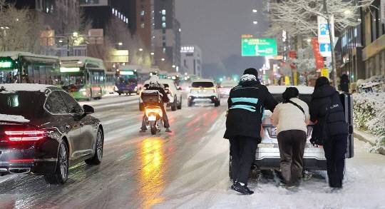 지난 4일 서울 마포구 홍대 인근에서 제설작업이 완료되지 못한 도로에서 시민들이 언덕길 차를 밀고 있다. 연합뉴스