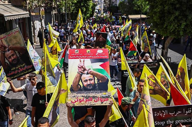 지난 8월 19일(현지시간) 팔레스타인 자치정부(PA)의 집권 정파인 파타(Fatah)의 핵심 인사이자 이스라엘 구금 중인 최고위급 팔레스타인 수감자 마르완 바르구티를 지지하는 행진에서 시위 참가자들이 바르구티의 얼굴이 담긴 깃발과 피켓을 들어 올리고 있다. 유엔 인권사무소는 같은 날, 이스라엘 극우 성향의 이타마르 벤그비르 국가안보장관이 수감 중인 바르구티를 조롱하는 행위를 하고 그 영상을 온라인에 공유한 데 대해 규탄했다. AFP연합뉴스