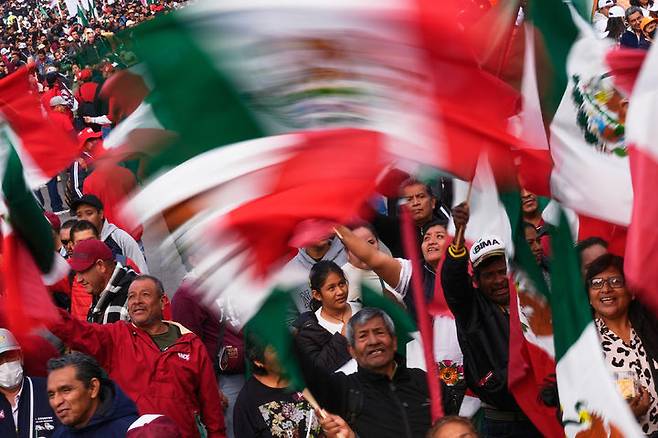 [멕시코시티= AP/ 뉴시스] 멕시코시티에 모인 클라우디아 세인바움 대통령의 지지자들이 여당의 집권 7주년을 기념하는 군중대회에서 국기를 흔들며 축하하고 있다.  이 날 미초아칸 주에서는 주지사가 이 행사에 참석하는 동안 6일 코아후아야나 시 경찰서에서 폭발물이 터져 9명의 사상자가 발생했다. 2025. 12. 07.