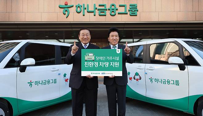 Hana Financial Group Chairman Ham Young-joo, right, poses for a photo with Kim Sung-yi, president of the Korea National Council on Social Welfare, during a vehicle donation ceremony at the group’s headquarters in Myeongdong, central Seoul, on Dec. 8. Hana Financial donated environmentally friendly vehicles to 10 assisted living residences to improve transportation access and welfare services. [HANA FINANCIAL GROUP]