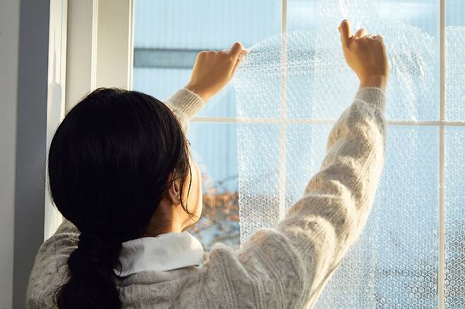 주거 공간의 열 손실을 줄이기 위해 창문에 에어캡을 부착하는 모습. 클립아트코리아