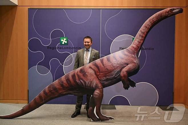 16일(현지시간) 밀라노-코르티나 2026 동계올림픽 개최 예정지 인근인 스텔비오 국립공원에서 발견된 수천 개의 공룡 발자국 사진이 이탈리아 롬바르디아주 청사에서 열린 기자회견에서 공개됐다. 국립공원 관할 책임자인 프랑코 클라레티 국장이 종이로 만든 공룡 모형과 함께 서 있다. 2025.12.16. ⓒ AFP=뉴스1 ⓒ News1 윤다정 기자