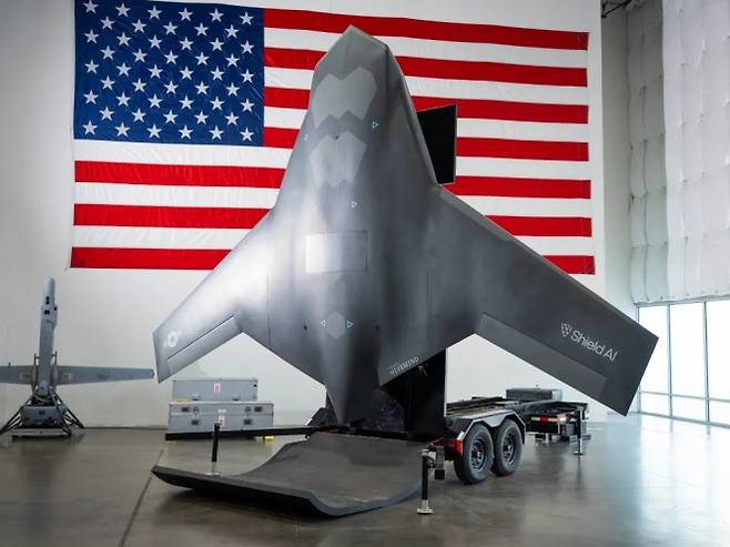 미국 국기 아래 전시된 차세대 전투 드론 ‘엑스밧’ 모형. 출시 트레일러 위에 설치된 형태로, 왼쪽에는 실드AI의 기존 수직이착륙 드론 ‘브이밧’이 함께 보인다. 사진=실드AI