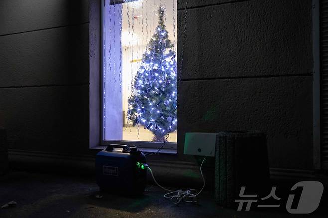 22일(현지시간) 우크라이나 남부 도시 오데사에서 러시아의 미사일과 드론 공격으로 에너지 시설이 파괴돼 정전이 이어지는 가운데 한 주택 앞에 발전기가 놓여 있고 크리스마스 트리가 장식돼 있다.2025.12.22.ⓒ AFP=뉴스1