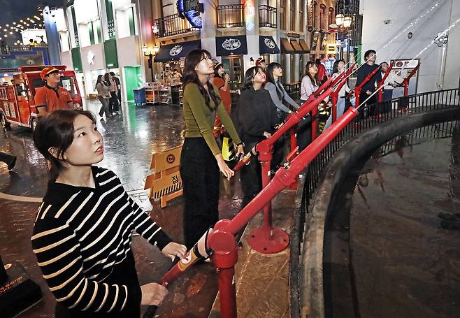 A cohort of eight adults, including this reporter, left, assume the role of firefighters, spraying water from a hose at a structure that appears to be engulfed in flames at KidZania in Jamsil, southern Seoul, on Dec. 20. [PARK SANG-MOON]