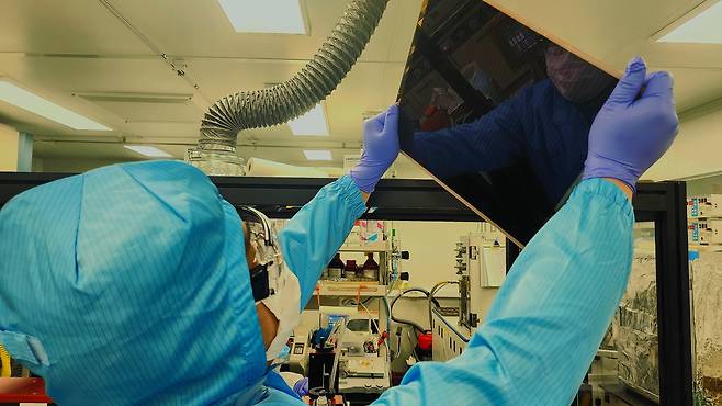 한국화학연구원에서 기술을 이전받아 상용화를 위해 협업중인 (주)엘케이켐 연구원이 대면적 페로브스카이트 태양전지 기판을 보고있다.[한국화학연구원 제공]