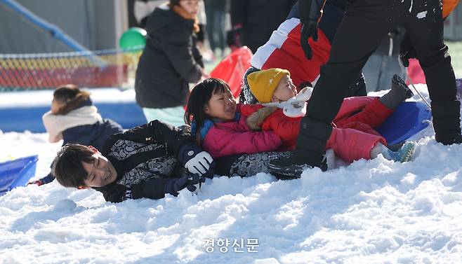 어린이들이 아버지가 끌어주는 눈썰매를 타던 중 넘어지고 있다.