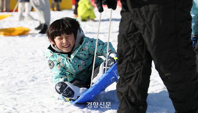 한 어린이가 아버지가 끌어주는 썰매를 타며 미소짓고 있다.