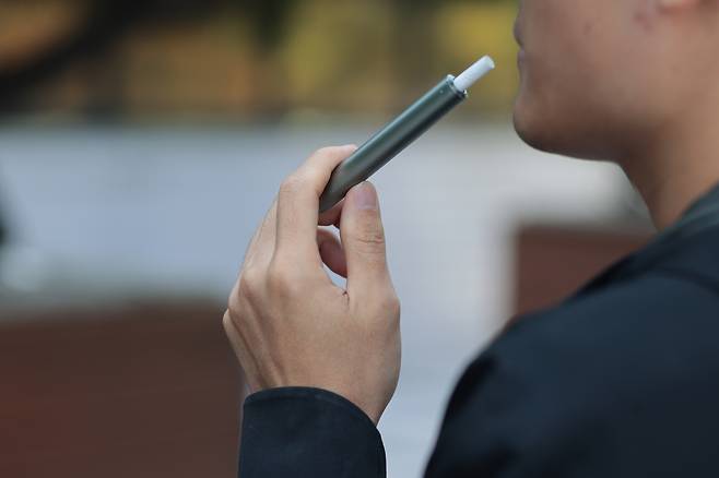 A person is seen smoking an e-cigarette at a smoking zone in Seoul on June 12. [YONHAP]