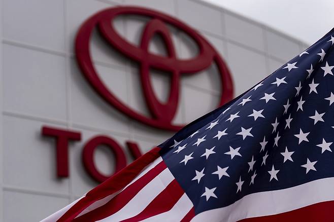 An American flag flutters in the wind in front of a Toyota logo at a dealership in Cerritos, California on March 27. [AP/YONHAP]