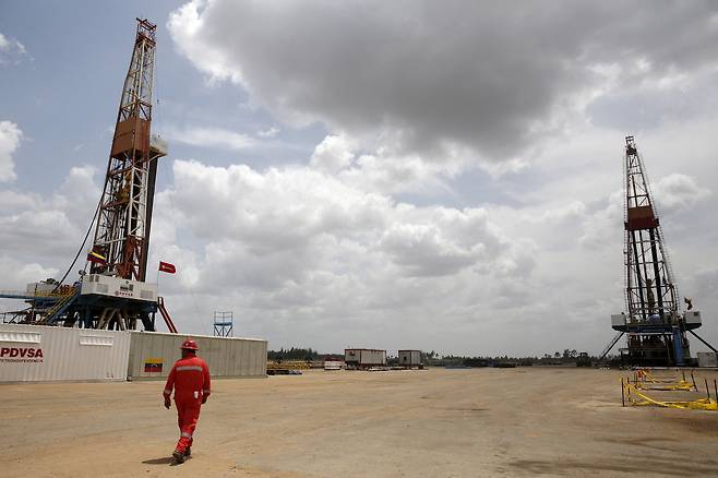 An oilfield worker walks next to drilling rigs at an oil well operated by Venezuela's state oil company PDVSA, in the oil rich Orinoco belt, near Morichal at the state of Monagas, April 16, 2015. [REUTERS/YONHAP]