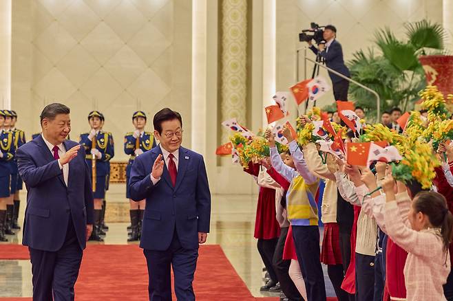 Korean President Lee Jae Myung, right, and Chinese President Xi Jinping wave to children during an official welcoming ceremony at the Great Hall of the People in Beijing before their bilateral summit on Jan. 5. [JOINT PRESS CORPS]
