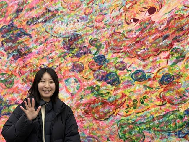 아야코 록카쿠 작가가 토탈미술관에 전시된 자신의 작품 앞에서 손을 들고 웃고 있다.