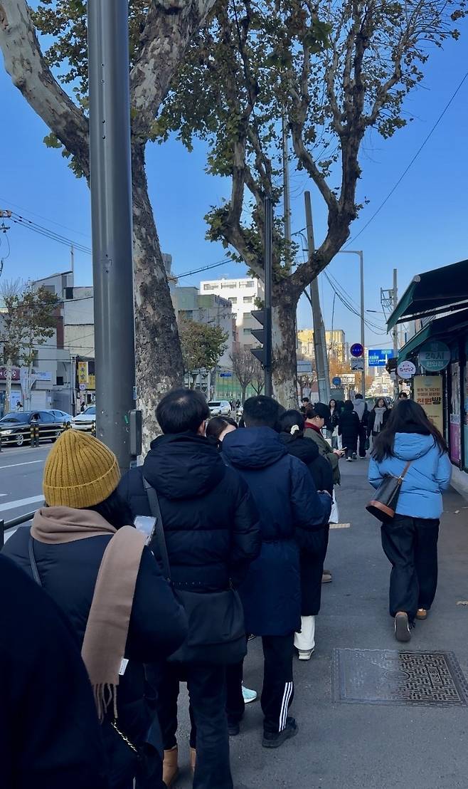 A line snakes down the sidewalk outside the Namyeong Station bungeoppang shop, where waiting 30 minutes to over an hour for a street snack has become routine. (Moon Joon-hyun/The Korea Herald)