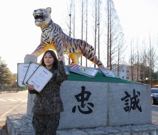 2기갑여단 적오대대 이나라 중사가 부대를 상징하는 호랑이상 앞에서 머리카락 기부증서를 들고 화이팅 포즈를 취하고 있다. 2기갑여단 제공