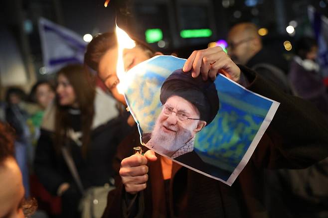 14일(현지시각) 이스라엘 홀론에서 열린 이란 반정부 시위를 지지하는 시위가 열린 가운데 한 이스라엘 거주 이란 여성이 이란 최고지도자 아야톨라 알리 하메네이의 사진에 불을 붙이고 있다. EPA 연합뉴스…