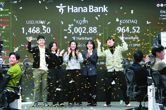 Currency traders celebrate as they work in the office with a screen showing the Kospi, center, of over 5,000 points at the foreign exchange dealing room of the Hana Bank headquarters in central Seoul on Thursday. [AP/ YONHAP]