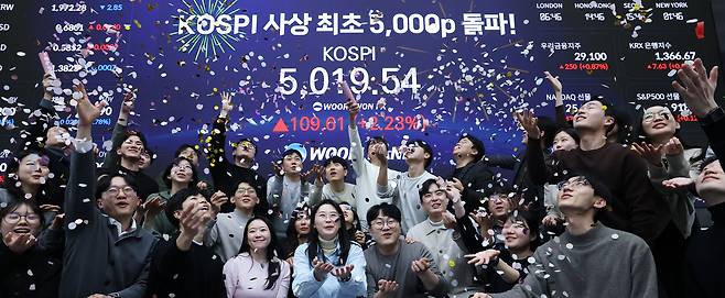 한국 증시가 장중 사상 처음으로 '코스피 5000' 쾌거를 달성한 22일 서울 중구 우리은행 본점 딜링룸에서 직원들이 장중 최고가가 찍힌 전광판을 배경으로 코스피 5000 돌파를 축하하고 있다. 이날 코스피는 이재명 대통령이 '코스피 5000' 공약을 내걸고 임기를 시작한 지 7개월 만에 꿈의 5000을 돌파하며 한국 자본시장의 역사를 새로 썼다. /뉴스1