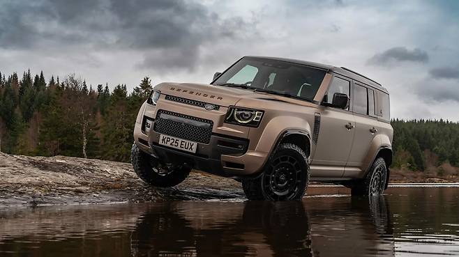 숲속 물가에 정차해 잇는 유니크한 브론즈 색상의 랜드로버 디펜더 옥타 측면 사진