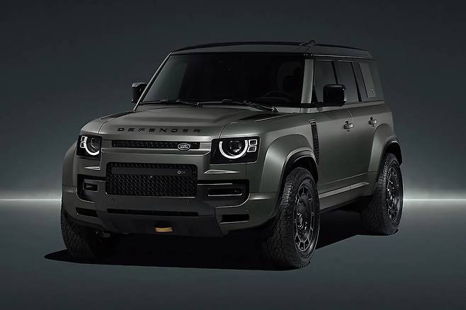 어두운 스튜디오 배경에서 강렬한 전면부 디자인과 헤드램프를 강조한 다크 그레이 랜드로버 디펜더 옥타 정면샷