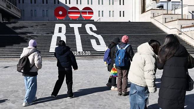 지난달 22일 서울 종로구 세종문화회관 계단에서 외국인 관광객들이 오는 3월 3년 9개월 만에 '완전체'로 돌아오는 그룹 방탄소년단(BTS)의 컴백을 알리는 홍보물을 기념촬영하고 있다. 연합뉴스